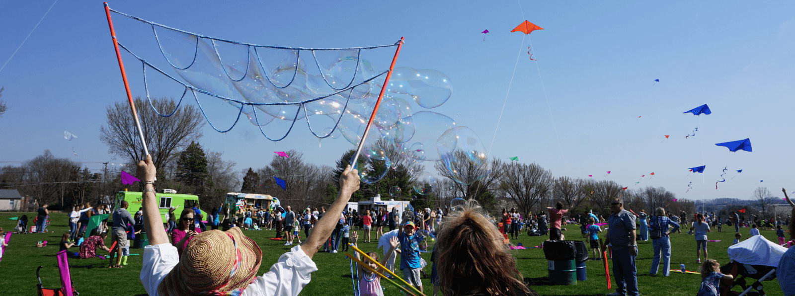 Person holding up bubble maker in a crowd of people flying kites in a field