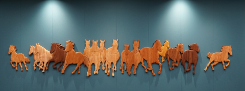 A wood sculpture displayed against the wall of galloping horses.