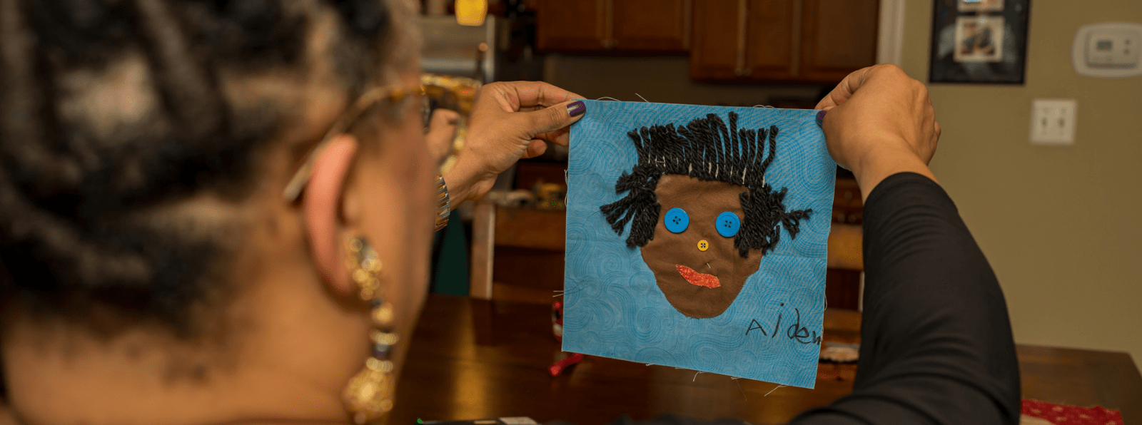 A person holding up a collage portrait labeled “Aiden.”