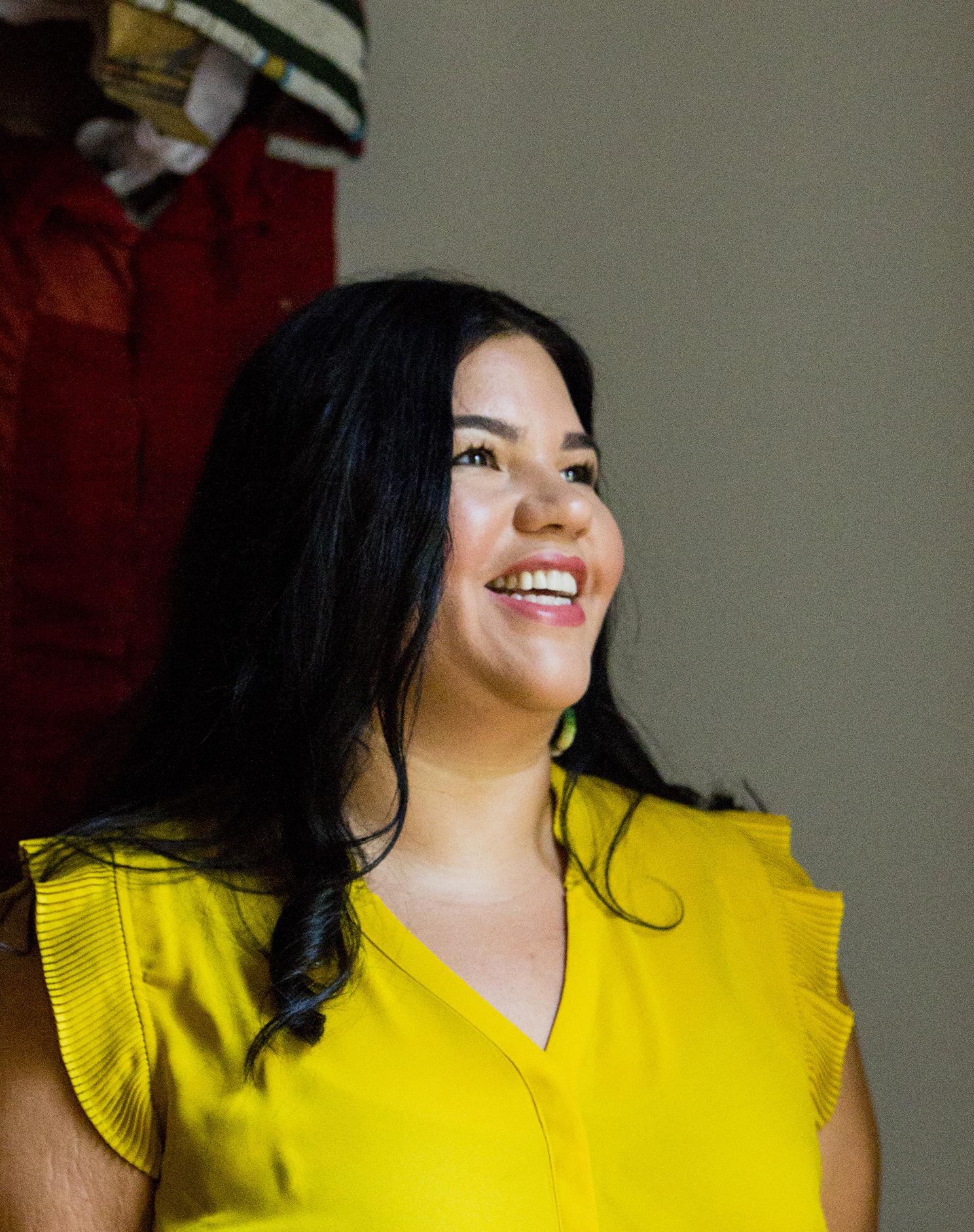 Dark-haired woman in a yellow shirt smiling and looking off to the side.