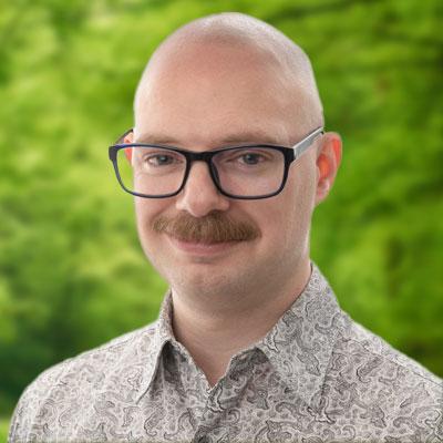 Ryan Koons headshot. Man smiling with dark glasses and a multicolored shirt.