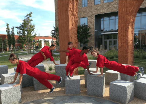 Four dancers in jumpsuits lay across a concrete public art display
